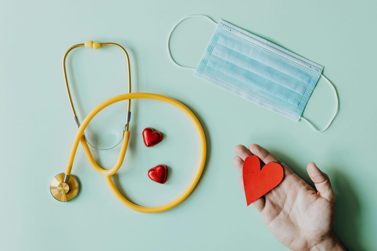 Yellow looped stethoscope with two small red hearts at the center and a hand holding a heart shape.