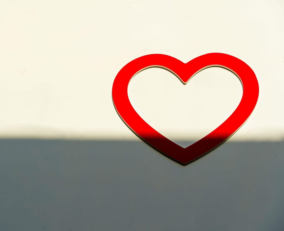 Red heart shape outline on beige wall with a shadow casting halfway on it.